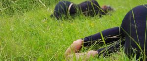 Partecipanti raggomitolati e distesi a pancia in giù nell'erba alta durante un bagno di foresta e meditazione fetale, tecniche di meditazione Bodhi Vipal al Centro Zorba Il Buddha.