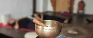 Campana tibetana in primo piano con batacchio in legno e partecipante disteso a terra sullo sfondo in rilassamento profondo, tecniche di meditazione Bodhi Vipal al Centro Zorba Il Buddha.