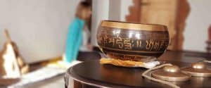 Campana tibetana decorata in primo piano con tingsha e partecipante seduta a terra sullo sfondo durante un ritiro di meditazione Vipassana, tecniche di meditazione Bodhi Vipal al Centro Zorba Il Buddha.