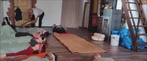 Partecipanti distesi supini a terra con bende sugli occhi mentre l'operatore olistico suona un tamburo sciamanico sopra di loro durante un bagno sonoro di purificazione, tecniche di meditazione Bodhi Vipal al Centro Zorba Il Buddha.