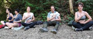 Cinque persone sedute a occhi chiusi nel bosco con una mano sul cuore e una sulla pancia per l'attivazione degli intenti, tecniche di meditazione Bodhi Vipal al Centro meditazione Zorba Il Buddha.