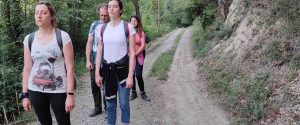 Quattro persone con zaini leggeri colte in piedi a occhi chiusi durante una sosta di presenza mentale lungo un sentiero sterrato nel bosco, in un ritiro di meditazione camminata con le tecniche di Bodhi Vipal al Centro Zorba Il Buddha.