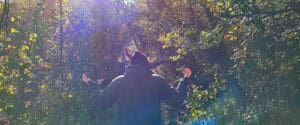 Gruppo di persone di spalle con le braccia aperte che cammina lungo un sentiero nel bosco illuminato dal sole, durante un'attività di meditazione camminata e riconnessione con la natura.