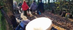 Tamburo sciamanico in primo piano nel bosco con gruppo di persone sedute in cerchio sullo sfondo durante un ritiro di Shinrin-Yoku, tecniche di meditazione Bodhi Vipal al Centro Zorba Il Buddha.