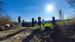 Gruppo di persone in piedi in cima a una collina con le mani unite sopra la testa rivolte verso il sole durante un ritiro di meditazione all'aperto al Centro Zorba Il Buddha.