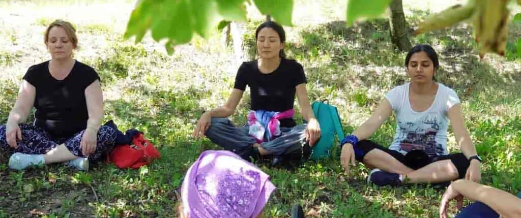 Tre donne che meditano sedute sul prato all'ombra di un albero in un parco.