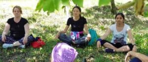 Tre donne che meditano sedute sul prato all'ombra di un albero in un parco.
