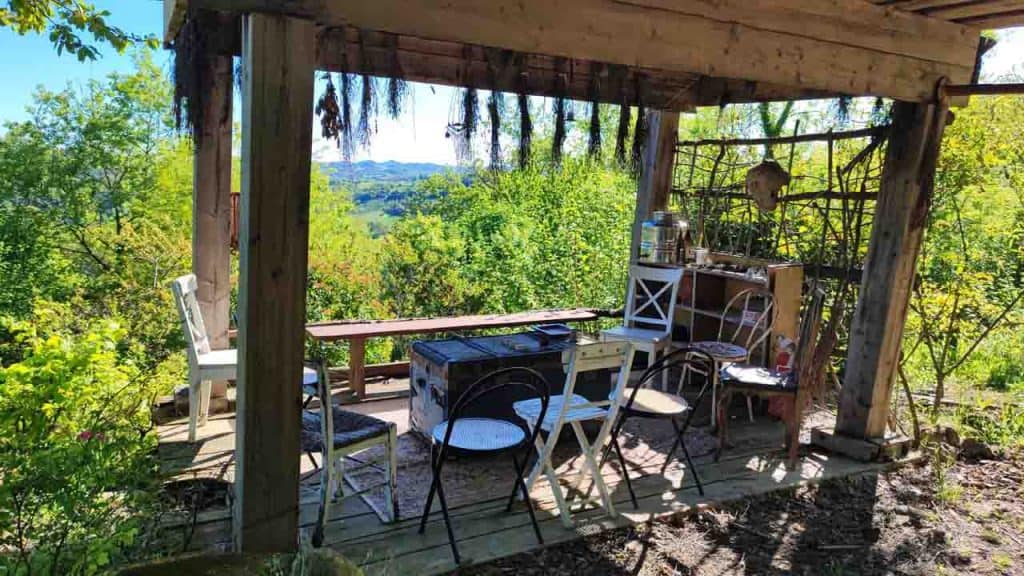 Gazebo in legno panoramico immerso nel verde con sedie disposte a cerchio, erbe aromatiche essiccate appese alle travi e vista sulle colline al Centro Zorba Il Buddha.