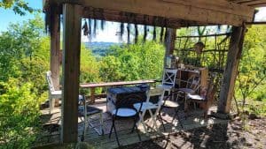 Gazebo in legno panoramico immerso nel verde con sedie disposte a cerchio, erbe aromatiche essiccate appese alle travi e vista sulle colline al Centro Zorba Il Buddha.